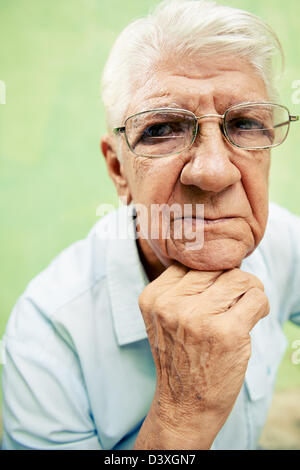 people and emotions, portrait of depressed senior hispanic man with glasses looking at camera, leaning with hands on chin Stock Photo