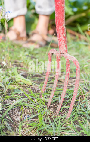 Garden fork with feet of gardener in the background Stock Photo