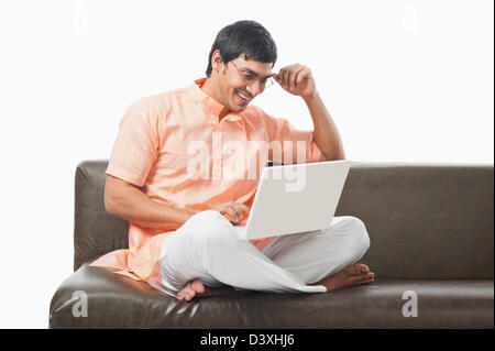 Bengali man using a laptop on the couch Stock Photo