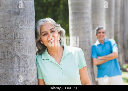 Woman leaning against a tree with her husband in the background, Lodi Gardens, New Delhi, India Stock Photo