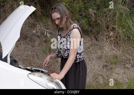 A young adult woman uses a screwdriver to fix her broken down car. Stock Photo
