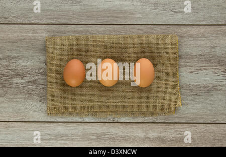 Three brown chicken eggs on burlap and weathered boards Stock Photo