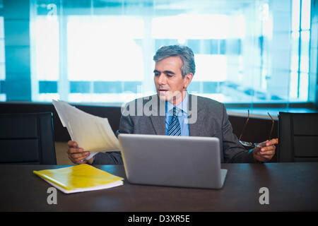 Businessman sitting in front of laptop reading documents Stock Photo