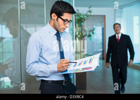Businessman reading a report with his boss in the background Stock Photo