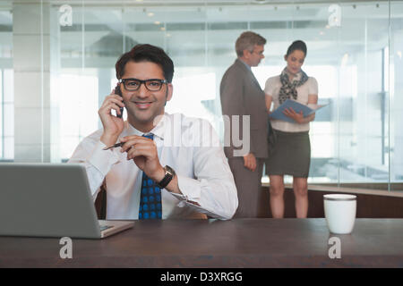 Businessman talking on a mobile phone with their colleagues standing in the background Stock Photo