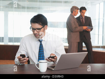 Businessman using a mobile phone with their colleagues standing in the background Stock Photo