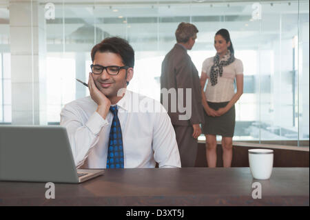 Businessman looking at a laptop with their colleagues standing in the background Stock Photo