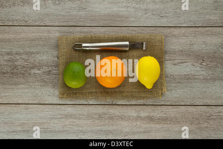 A group of three different citrus fruits lined up next to each other (lime, orange, lemon) with zester tool Stock Photo