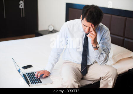 Worried businessman using a laptop on the bed Stock Photo