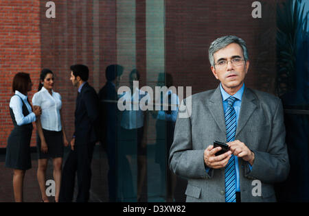 Businessman using a mobile phone with their colleagues talking in the background Stock Photo