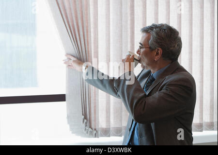 Businessman looking out through from a window and drinking coffee Stock Photo