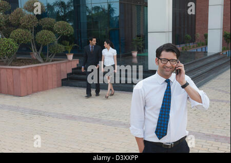 Businessman talking on a mobile phone with their colleagues in the background Stock Photo