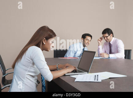 Two businessmen looking at their colleague working on a laptop Stock Photo