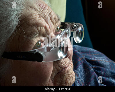 Macular degeneration elderly old senior lady with visual impairment  eye sight wearing special magnifying glasses to watch television in her room Stock Photo