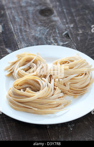 Homemade fettuccini noodles rolled into nests on white plate Stock Photo