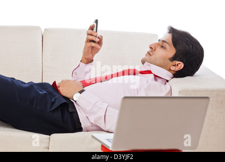 Businessman lying on a couch and using a mobile phone Stock Photo