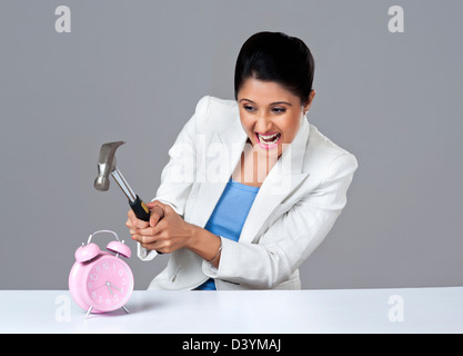 Businesswoman smashing alarm clock with hammer Stock Photo