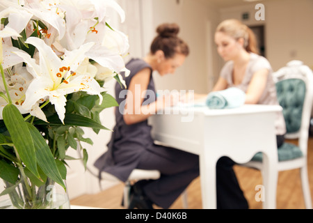 A young woman having her nails painted in a beauty salon. The subjects are in the background with a vase of flowers to the left Stock Photo