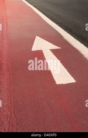 White straight ahead one way direction arrow road markings painted on a red road surface, UK Stock Photo