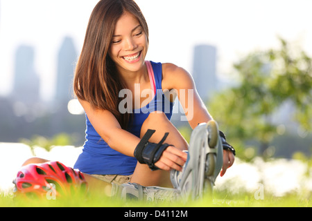 Happy young woman putting on inline skates for rollerblading with Montreal city skyline in background Stock Photo