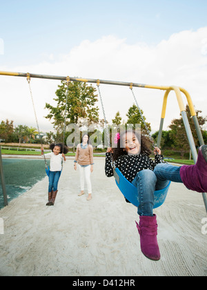 Mother pushing daughters on swings Stock Photo