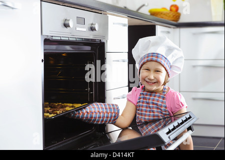 Cute little girl in kitchen mitten put cookies in stove Stock Photo