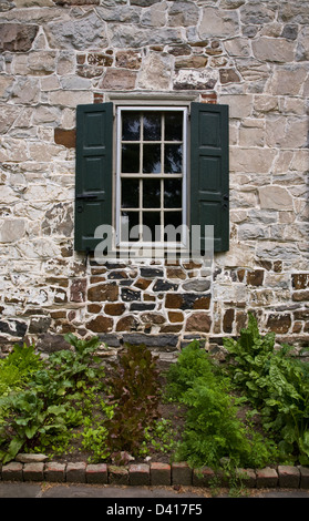 Historic stone house window kitchen spring herb garden in Lancaster County, Pennsylvania, USA, pt crops, storm shutters, close up vegetable garden Stock Photo