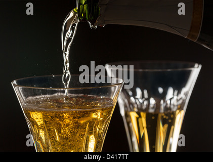 Detail of a pair of cut glass champagne goblet with a heart on the side and drink being poured Stock Photo