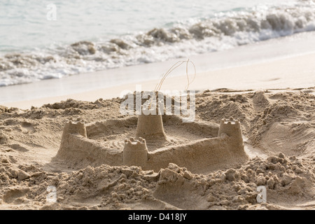 Sandcastle built in sand by sloping sandy beach to surf by ocean Stock Photo