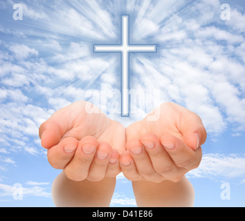 Hands holding Christian cross with light beams over sky Stock Photo