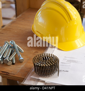 Nails and a hard hat sitting on top of blueprints or plans at a construction site Stock Photo