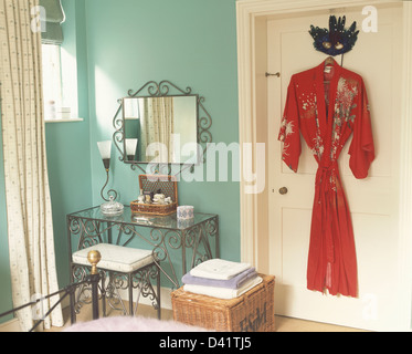 Ornate metalwork dressing table with matching stool and mirror in turquoise bedroom with red silk kimono on door Stock Photo