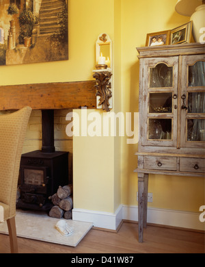 Corbel with candle on wall beside cast-iron wood-burning stove in yellow dining room with lime-washed glass-fronted cupboard Stock Photo