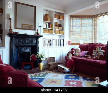 Small girl lying and reading on red velvet sofa beside her brother reading a book in townhouse living room Stock Photo