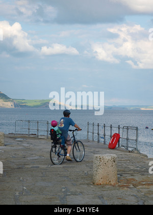 Father and child on one bicycle pause to look out to sea at the harbour Stock Photo