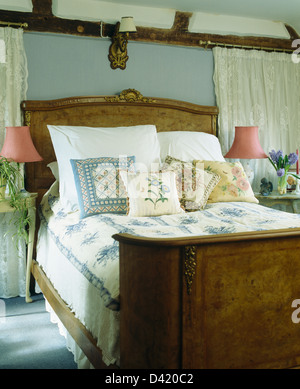 White pillows and patterned cushions on antique burr-walnut bed with blue+white quilt in gray blue bedroom Stock Photo