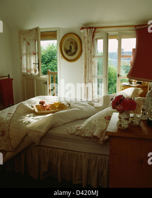 Breakfast tray on bed with floral+spotted quilt in French country bedroom with view of the garden through open window Stock Photo