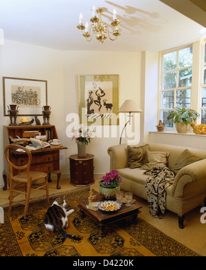 Cat lying on oriental rug in front of beige sofa in cottage living room with antique bureau and chair Stock Photo
