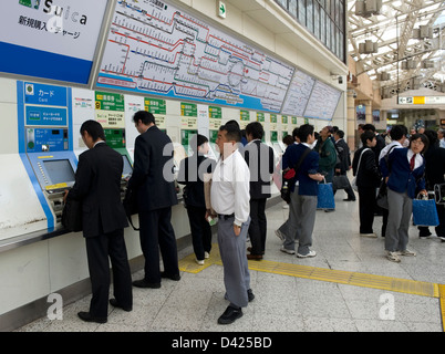 Businessmen, students and other commuters purchasing train tickets from vending machines inside Ueno Station, Tokyo. Stock Photo