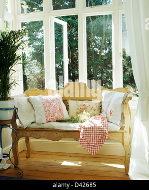 White linen cushions on pine settle in front of French windows in country living room Stock Photo