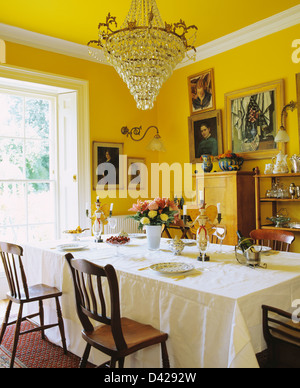 Large antique glass chandelier above table set with crisp white cloth in yellow country dining room Stock Photo