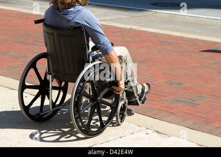 Injured male veteran sitting in his wheelchair rolls on the sidewalk. Stock Photo