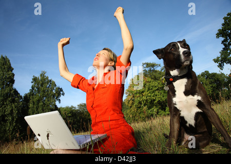 Berlin, Germany, a woman sitting with her laptop on the meadow and is relieved beside her dog Stock Photo