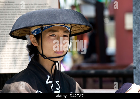 A jinrikisha (rickshaw) runner in traditional hat and kimono at a Tokyo tourist attraction waits for a customer. Stock Photo