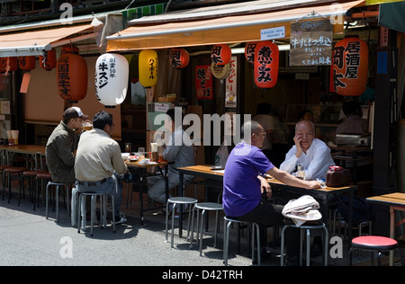 Patrons enjoying a beer or two at a street-side izakaya, or casual drinking establishment, in the working-class neighborhood Stock Photo