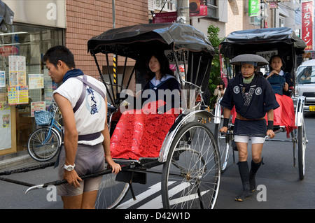 Sightseers taking a ride in a jinrikisha (rickshaw) through the streets of Asakusa, Tokyo, the old entertainment district. Stock Photo