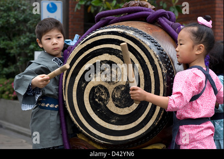 A boy and girl in festival attire join in the fun by beating a taiko drum during the Sanja Matsuri Festival in Tokyo. Stock Photo