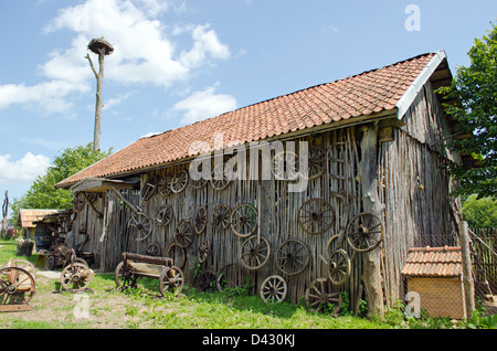 retro carriage wheel hang on rural barn house. wooden benches. stork nest on top. Stock Photo