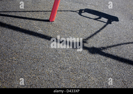 Shadow cast by the sun on the ground from an empty swing in a childrens playground. Stock Photo