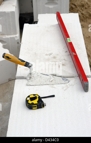 Mason's trowel, level and measuring tape on white hollow bricks Stock Photo